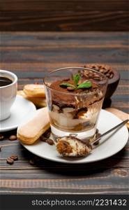Portion of Classic tiramisu dessert in a glass, cup of coffee and savoiardi cookies on wooden background or table. Portion of Classic tiramisu dessert in a glass, cup of coffee and savoiardi cookies on wooden background