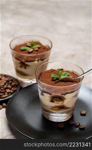 Portion of Classic tiramisu dessert in a glass cup on concrete background or table. Portion of Classic tiramisu dessert in a glass cup on concrete background