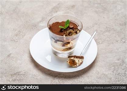 Portion of Classic tiramisu dessert in a glass cup on concrete background or table. Portion of Classic tiramisu dessert in a glass cup on concrete background