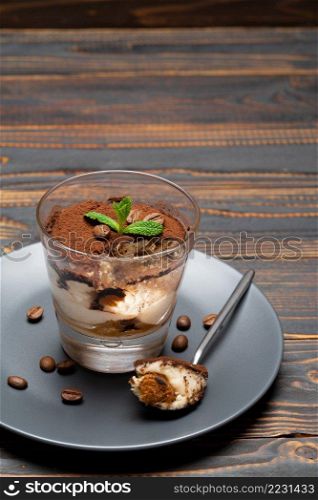Portion of Classic tiramisu dessert in a glass cup on wooden background or table. Portion of Classic tiramisu dessert in a glass cup on wooden background