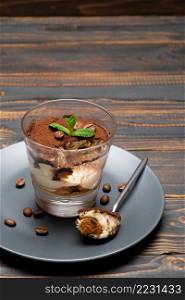 Portion of Classic tiramisu dessert in a glass cup on wooden background or table. Portion of Classic tiramisu dessert in a glass cup on wooden background