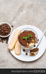 Portion of Classic tiramisu dessert in a glass, savoiardi cookies and cup of coffee on concrete background or table. Portion of Classic tiramisu dessert in a glass, savoiardi cookies and cup of coffee on concrete background