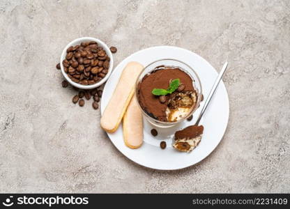 Portion of Classic tiramisu dessert in a glass, savoiardi cookies and cup of coffee on concrete background or table. Portion of Classic tiramisu dessert in a glass, savoiardi cookies and cup of coffee on concrete background