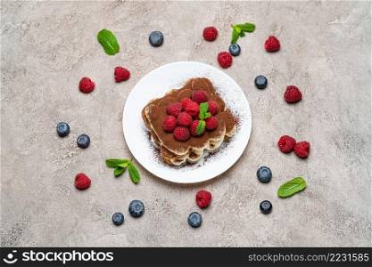 portion of Classic tiramisu dessert with raspberries and blueberries on grey concrete background or table. portion of Classic tiramisu dessert with raspberries and blueberries on grey concrete background