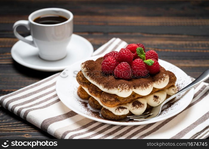 portion of Classic tiramisu dessert with raspberries and cup of espresso coffee isolated on wooden background or table. portion of Classic tiramisu dessert with raspberries and cup of espresso coffee isolated on wooden background