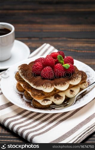 portion of Classic tiramisu dessert with raspberries and cup of espresso coffee isolated on wooden background or table. portion of Classic tiramisu dessert with raspberries and cup of espresso coffee isolated on wooden background