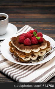 portion of Classic tiramisu dessert with raspberries and cup of espresso coffee isolated on wooden background or table. portion of Classic tiramisu dessert with raspberries and cup of espresso coffee isolated on wooden background