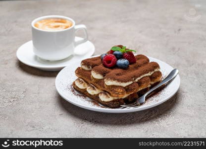 portion of Classic tiramisu dessert with raspberries, blueberries and cup of coffee on grey concrete background or table. portion of Classic tiramisu dessert with raspberries, blueberries and cup of coffee on grey concrete background