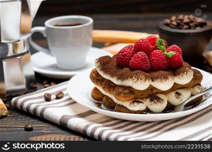 portion of Classic tiramisu dessert with raspberries, cup of espresso and coffee maker on wooden background or table. portion of Classic tiramisu dessert with raspberries, cup of espresso and coffee maker on wooden background
