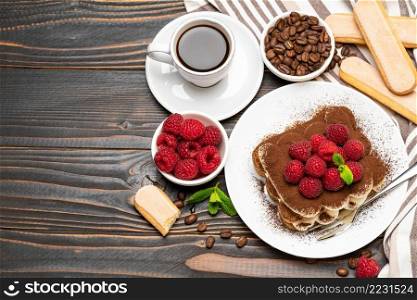 portion of Classic tiramisu dessert with raspberries, savoiardi cookies and cup of espresso coffee isolated on wooden background or table. portion of Classic tiramisu dessert with raspberries, savoiardi cookies and cup of espresso coffee isolated on wooden background