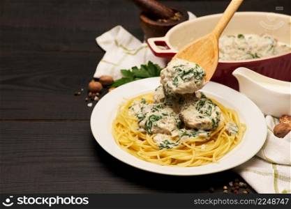 Portion of delicious meatballs with spinach in a creamy sauce and pasta on wooden background. High quality photo. Portion of delicious meatballs with spinach in a creamy sauce and pasta on wooden background