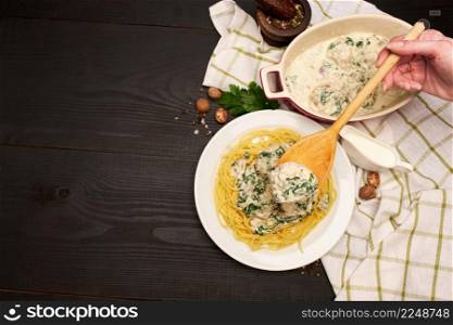 Portion of delicious meatballs with spinach in a creamy sauce and pasta on wooden background. High quality photo. Portion of delicious meatballs with spinach in a creamy sauce and pasta on wooden background