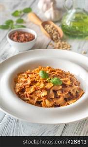 Portion of farfalle with sun-dried tomato pesto with ingredients on the white wooden table