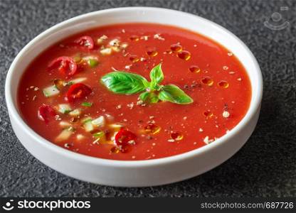 Portion of gazpacho garnished with fresh basil on the wooden table