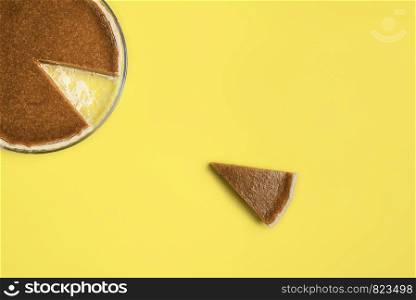 Portion of pie on yellow background. Pumpkin pie slice separated from the whole pie in a tray. Traditional dessert. Minimal and negative space image.