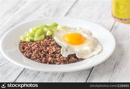 Portion of red quinoa with fried egg and celery on the wooden table