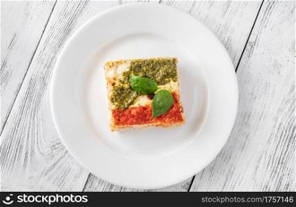Portion of ricotta lasagne topped with tomato sauce and pesto