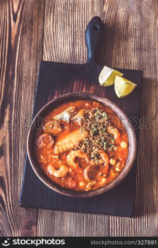 Portion of spanish fish and chorizo soup garnished with lemon wedges and pangrattato