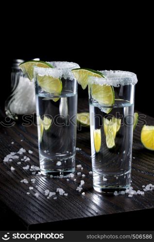 Portion of tequila, framed with a salt edge with slice lime in tall shot glasses
