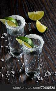 Portion of tequila, framed with a salt edge with slice lime in tall shot glasses
