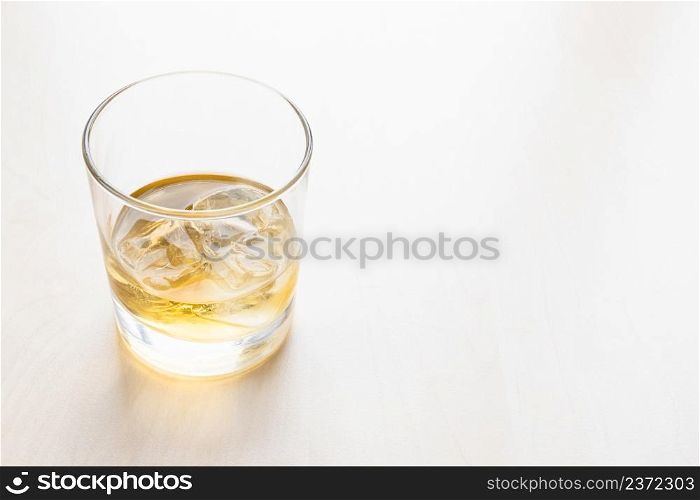 portion whiskey on the rocks in glass on pale table with copyspace