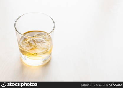 portion whiskey on the rocks in glass on pale table with copyspace