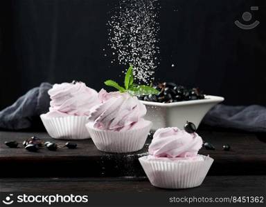 Portioned fruit marshmallows in a paper cup on a black wooden board, delicious dessert