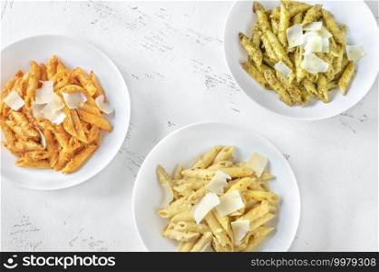 Portions of penne pasta with traditional, orange and yellow pesto sauce