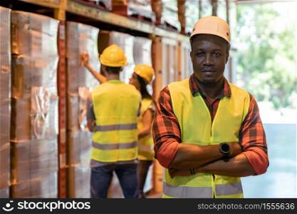 Portrait african black warehouse supervisor standing and crossed his arms in large warehouse distribution center with worker work on inventory in background. Business warehouse and logistic concept