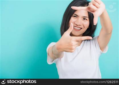 Portrait Asian beautiful happy young woman smile white teeth wear white t-shirt standing making creativity photography frame with hands and fingers, on a blue background with copy space