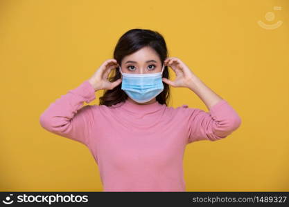 Portrait Asian beautiful happy young woman wearing face mask or protective mask against coronavirus crisis or COVID-19 outbreak on yellow background