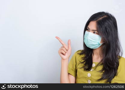 Portrait Asian beautiful happy young woman wearing face mask protects filter dust pm2.5 anti-pollution, anti-smog, and air pollution her pointing out to space on a white background, with copyspace