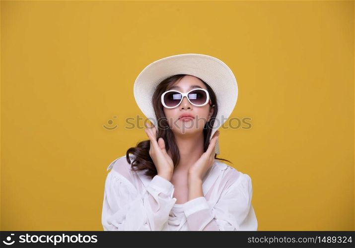Portrait Asian beautiful happy young woman with sunglasses and hat smiling cheerful in summer and looking at camera isolated on yellow studio background.