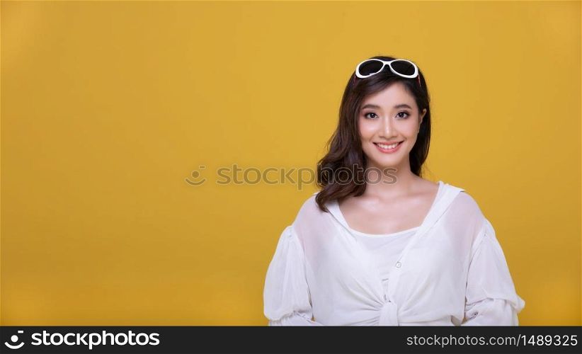 Portrait Asian beautiful happy young woman with sunglasses smiling cheerful and looking at camera isolated on yellow studio background.
