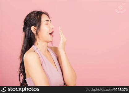 Portrait Asian beautiful young woman emotions tired and sleepy her yawning covering mouth open by hand, studio shot isolated on pink background, Thai female insomnia concept
