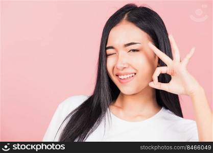 Portrait Asian beautiful young woman made finger OK symbol sign gesture wink eyes to agree and looking at camera, studio shot isolated on pink background, Thai female agree hand sign copy space