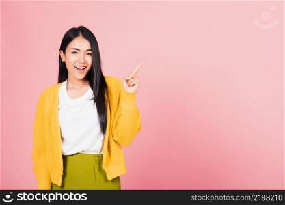 Portrait Asian beautiful young woman smiling standing pointing finger out on pink background, Thai happy face excited female point into empty looking to camera with copy space for text