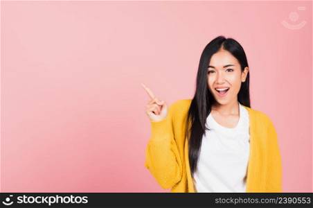 Portrait Asian beautiful young woman smiling standing pointing finger out on pink background, Thai happy face excited female point into empty looking to camera with copy space for text