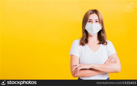 Portrait Asian beautiful young woman stand crossed arm wearing face mask protection filter dust pm2.5 anti-pollution, anti-smog, air pollution and COVID virus on a yellow background, with copy space