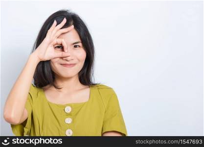 Portrait Asian beautiful young woman standing, She made finger OK symbol sign to agree near eye and looking at camera, shoot photo in studio on blue background, There was copy space