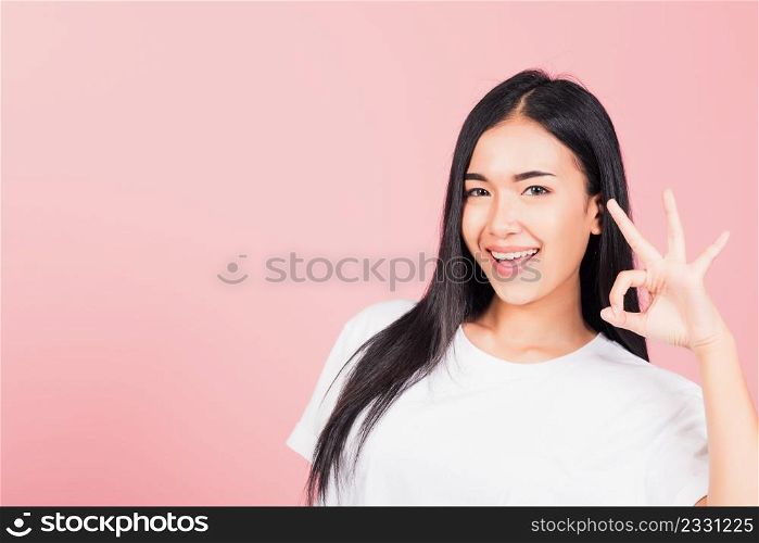 Portrait Asian beautiful young woman standing, She made finger OK symbol sign to agree side away looking at camera, studio shot isolated on pink background, Thai female agree hand sign copy space