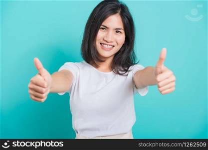 Portrait Asian beautiful young woman standing, She made finger thumbs up, Ok sign to agree and looking at camera, shoot photo in studio on blue background, There was copy space