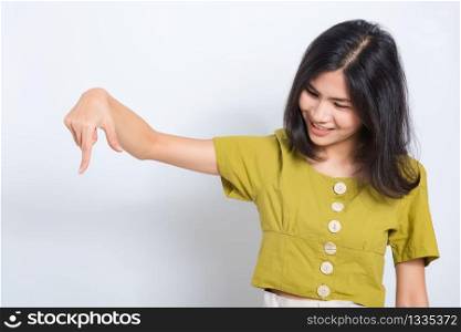 Portrait Asian beautiful young woman standing, She points down to space with fingers and looking to space, shoot photo in a studio on white background, There was copyspace