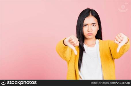 Portrait Asian beautiful young woman unhappy, negative gesture showing finger thumbs down or dislike sign, studio shot isolated on pink background, Thai female rejection unlike with copy space