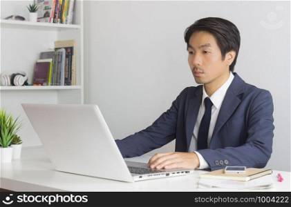 Portrait Asian Businessman in Formal Navy Blue Suit Using Laptop and Working in Office. Asian businessman with laptop and smartphone