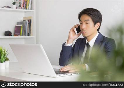 Portrait Asian Businessman in Formal Navy Blue Suit Working in Office and Using Smartphone and Laptop. Asian businessman with laptop and smartphone