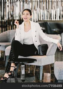 Portrait Asian businesswoman wearing formal suit sitting on the sofa in modern lobby, office or coworking space, coffee break leisure, fashion and lifestyle after working time,business people concept