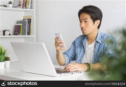 Portrait Asian Casual Businessman in Denim or Jeans Shirt Checking Mail and Chat with Colleague by Smartphone in Home Office. Casual businessman working with technology