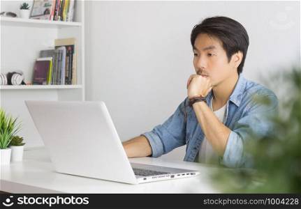 Portrait Asian Casual Businessman in Denim or Jeans Shirt Use Laptop and Thinking and Serious Pose in Home Office. Casual businessman working with technology