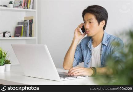 Portrait Asian Casual Businessman in Denim or Jeans Shirt Using Laptop and Smartphone in Home Office. Casual businessman working with technology